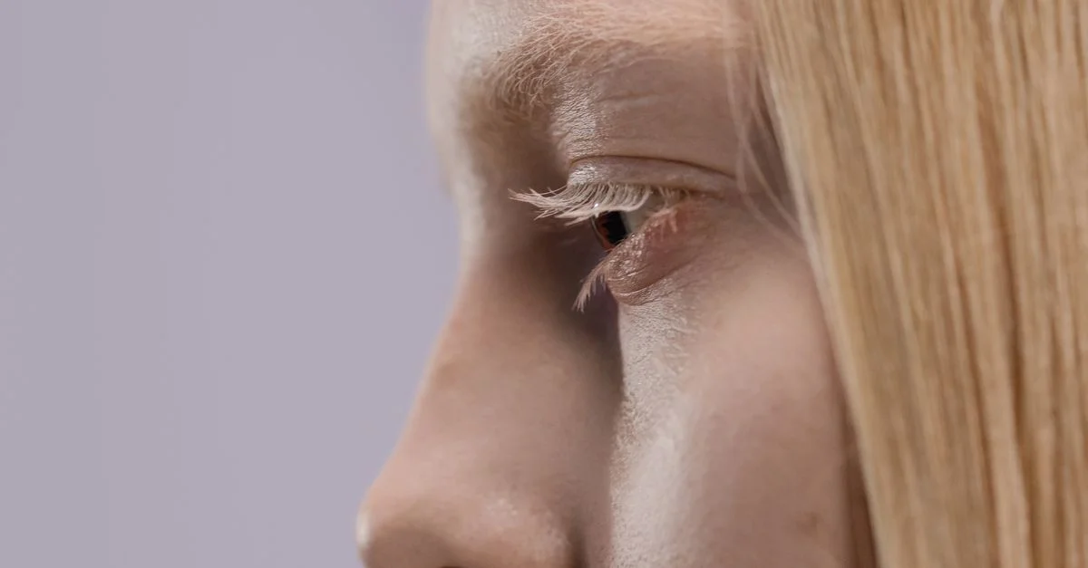 Vue de profil du visage d'une femme blonde, mettant l'accent sur l'œil et les cils dans un cadre minimaliste.