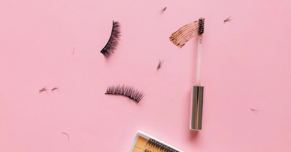 Mise en forme à plat de faux cils et pinceau de maquillage sur une surface rose pastel.